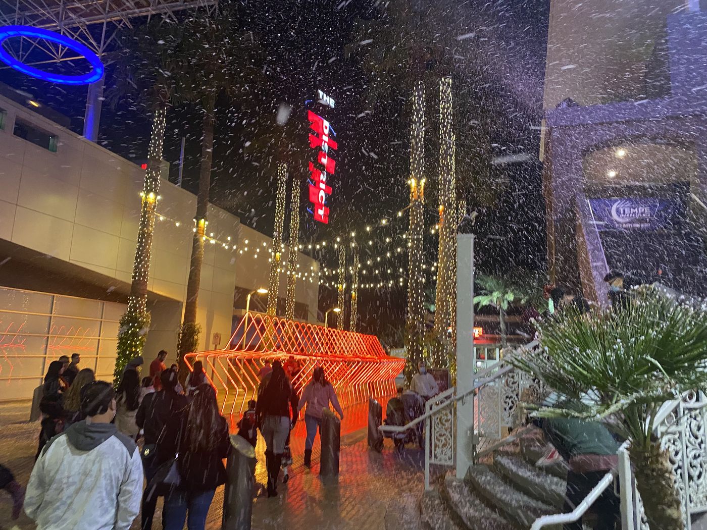 Snow falling over a lit outdoor plaza at night